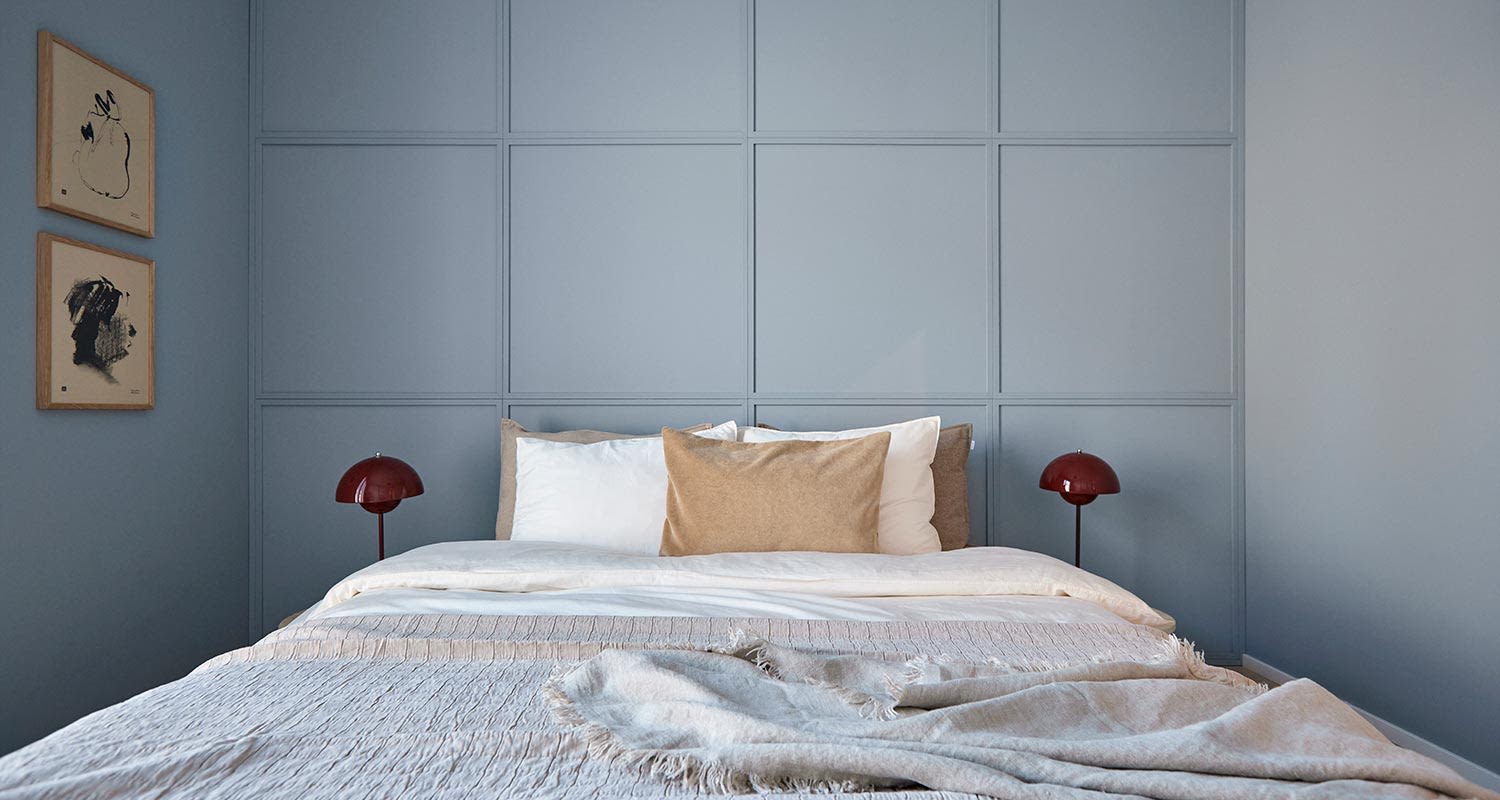 Makuuhuoneessa vaaleansininen paneeliseinä, valkobeige sänky, punaiset lamput, mustavalkoiset taulut.