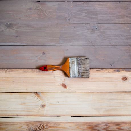 Oranssi sivellin maalaamassa puulautoja: ylälaidassa harmaa, alhaalla vaalea puu.
