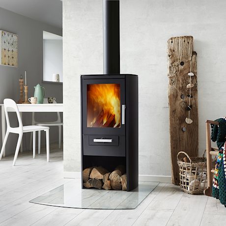 Musta takka liekein, polttopuut alaosassa, vaalea seinä ja rustiikki lankkukoriste