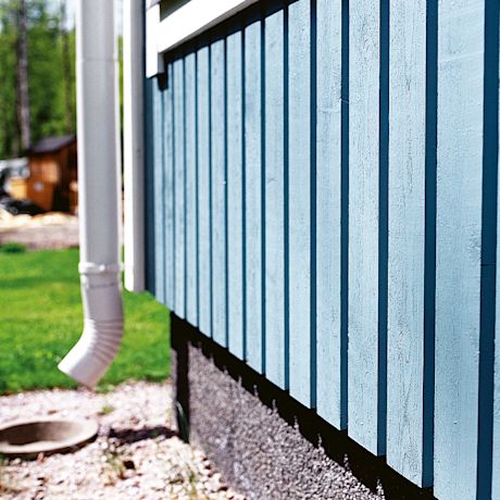 Vaaleansininen laudoitettu seinä ja valkoinen ränni nurmikon ja sorakivikön reunalla