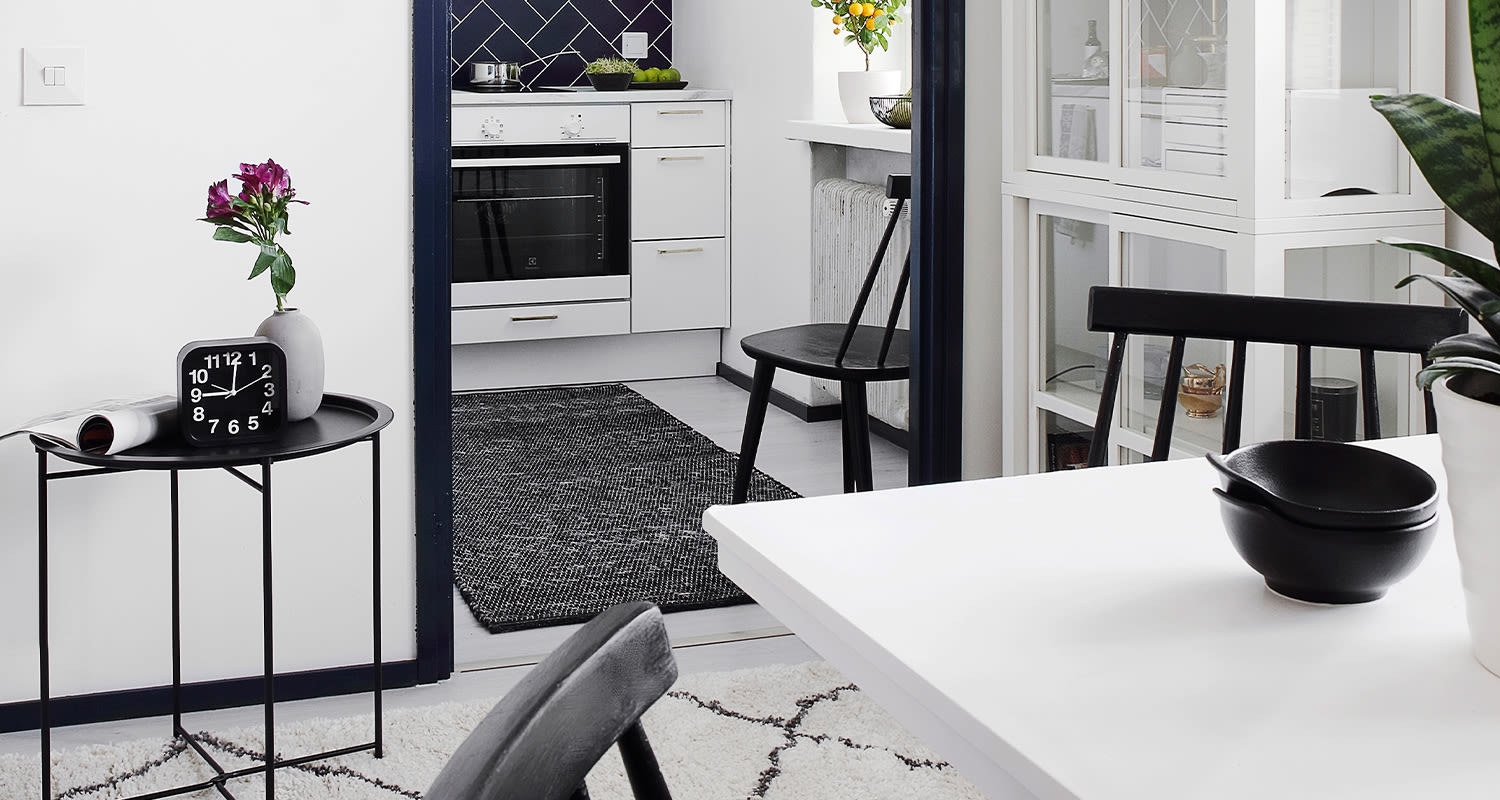 Valkois-musta skandinaavinen keittiö-ruokailuhuone, musta sivupöytä kellolla ja kukilla