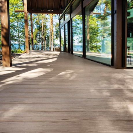 Moderni lasiseinäinen terassi järven rannalla, puupilarit, metsän vihreät varjot.