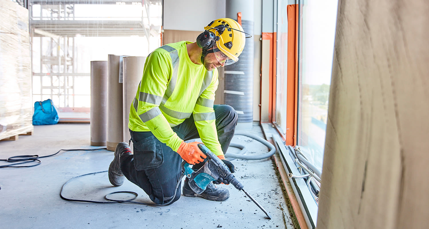 Rakennusmies käyttää Makitan piikkauskonetta Kalasataman rakennuskohteessa. Yllä työmiehellä on K-Raudan PROF Workwear -työvaatteet.