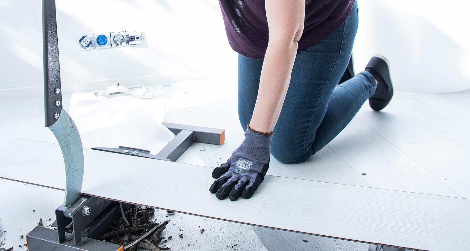 Nainen polvillaan leikkaa valkoista laminaattilautaa käsikäyttöisellä katkaisuleikkurilla.