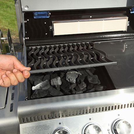 Käsi nostaa aaltokuvioista metalliritilää mustien hiilien päältä hopeisessa kaasugrillissä.