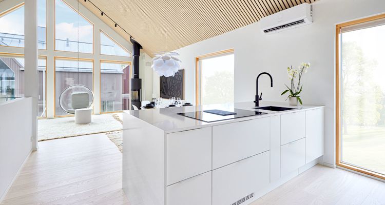 Valoisa avoin keittiö-olohuone valkoisella saarekkeella, musta hana ja suuret ikkunat