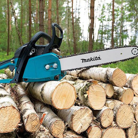 Turkoosi Makita-moottorisaha pinottujen koivupölkkyjen päällä havumetsässä