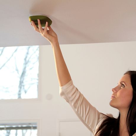 Henkilö asentaa vihreän pyöreän laitteen valkoiseen kattoon vaaleassa huoneessa.