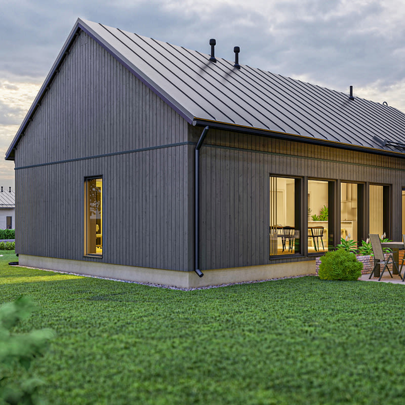 Moderni tumma puutalo harmaalla peltikatolla, keltainen sisävalo, vihreä nurmikko ja patioryhmä