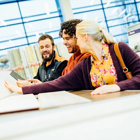 Nainen keltaisessa kukkapaidassa ja kaksi miestä valitsevat laattanäytteitä kirkkaassa myymälässä