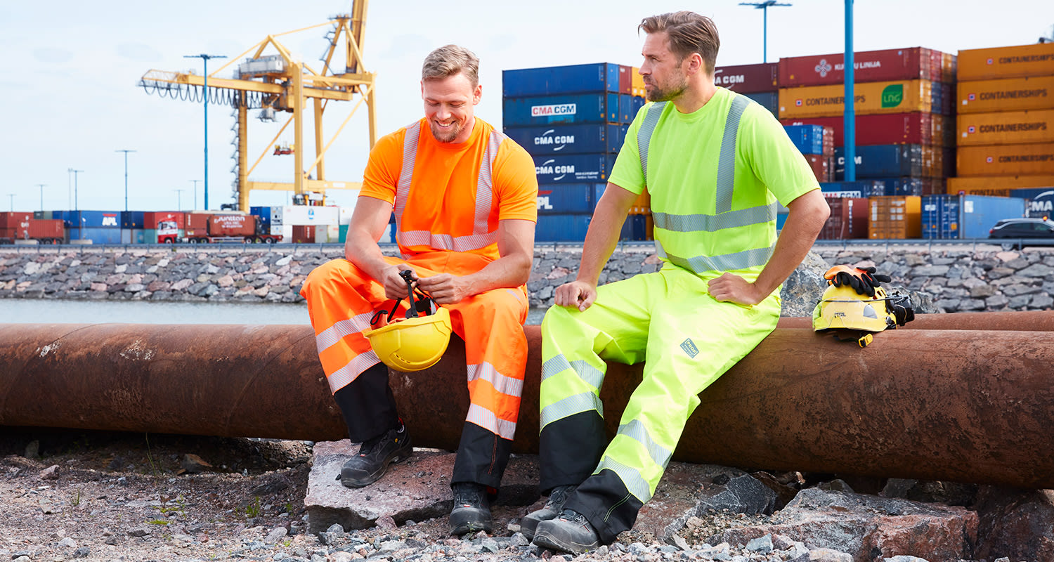 Kaksi rakennusmiestä Vuosaaren satamassa. Miehillä on yllä K-Raudann PROF Workwear -työvaatteet ja he viettävät taukoa.