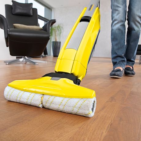Keltainen sähkömoppi pyörivillä rullilla parketilla olohuoneessa; henkilö sinisissä farkuissa.