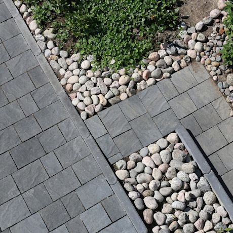 Ilmakuva harmaasta pihakiveyksestä: laatat, pyöreät kivet ja reunoissa vihreää kasvustoa.