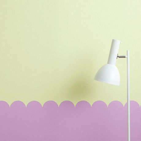 Valkoinen lattiavalaisin vaaleankeltaisen ja lilansävyisen aaltoilevaseinän edessä