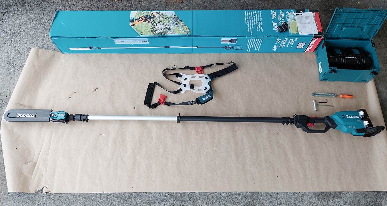 Ammattilaisen tuotetestin pakkaus, jossa Makitan akkuketjusaha akkupaketin kera. Kone näkyy maassa koottuna tarvikkeiden kera.