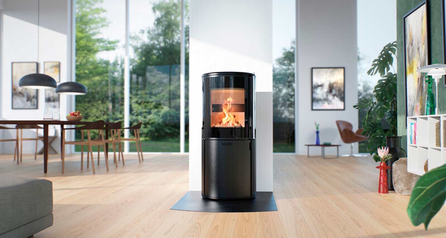 Musta pyöreä takka liekehtien puulattialla olohuoneessa valoisien ikkunoiden ja ruokapöydän edessä.