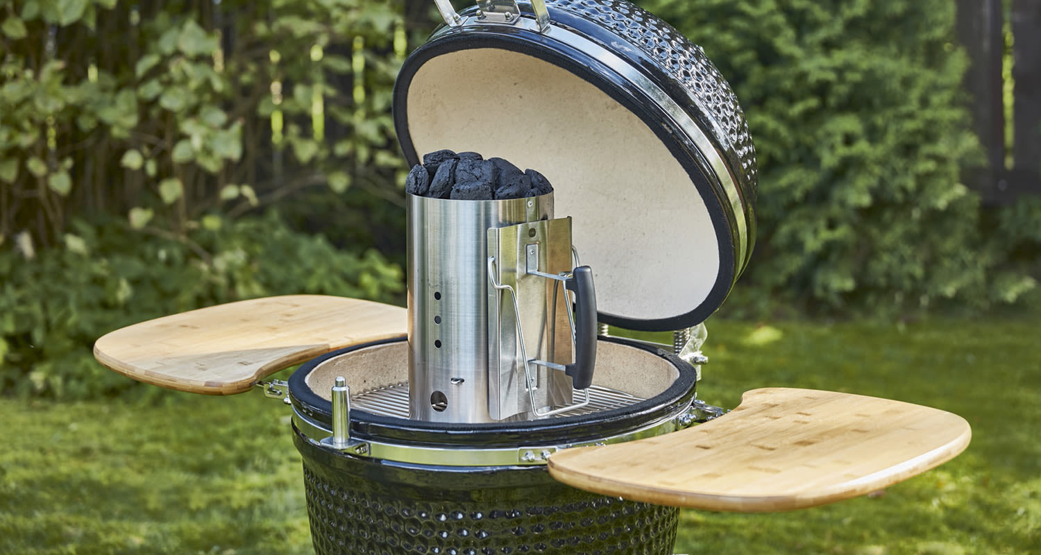 Avoin tummanvihreä kamadogrilli bambupöydillä ja teräspiipulla puutarhassa