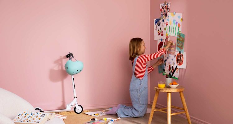 Vaaleanpunaisessa nurkassa lapsi kiinnittää piirustuksia seinälle, potkupyörä, välineet ja välipala