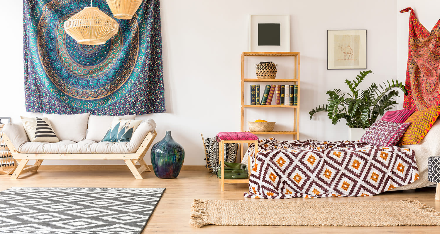 Boheemi olohuone: vaalea puusohva ja kuvioitu päivävuode mandalaverhon ja viherkasvin kera.