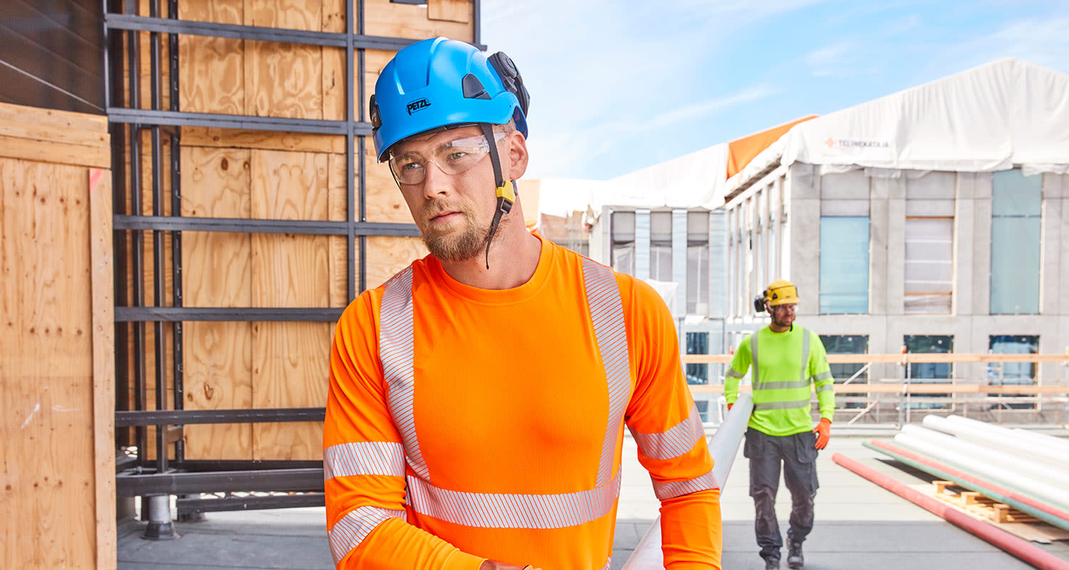 Työmiehet työmaalla PROF-työvaatteissa kantamassa putkea