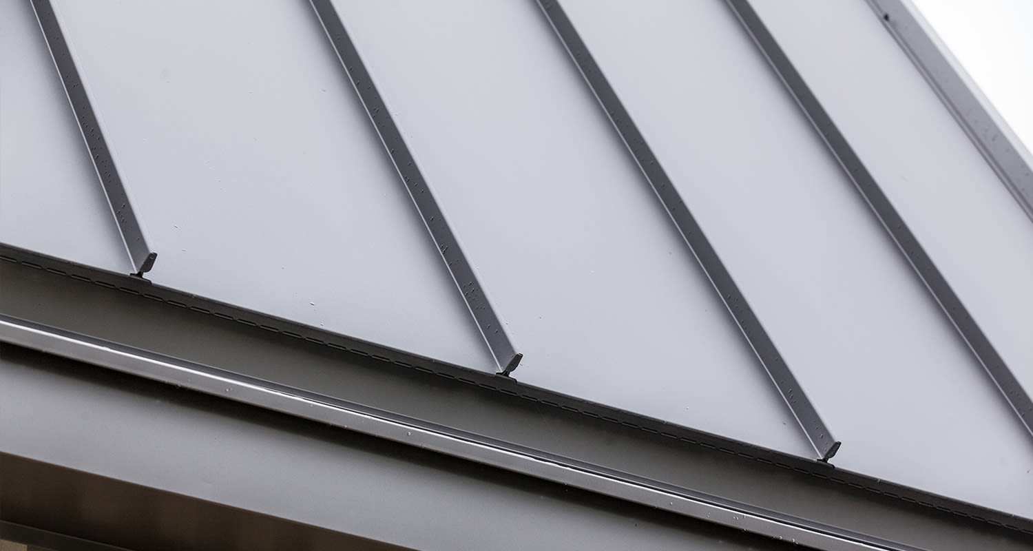 Vaaleanharmaa peltikaton vinokulmassa näkyviä pystysaumoja ja sadepisaroita