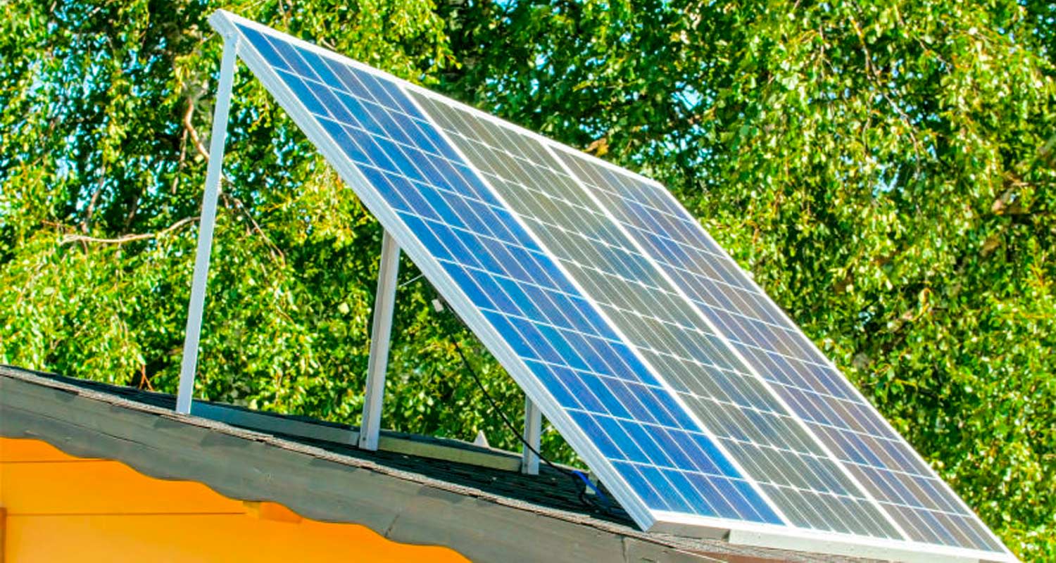 Sininen aurinkopaneeli kallistettuna talon katolla, vihreät puut taustalla.