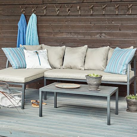 Terassilla beige-harmaa L-sohva vaaleansinisin tyynyin, metallipöytä ja seinällä peuranpääkoukut.