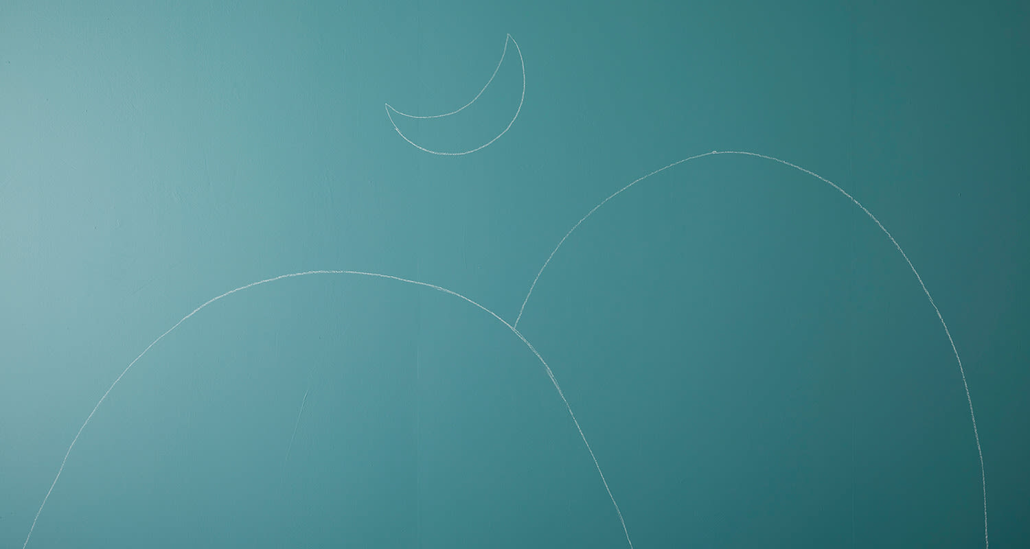 Vaaleanturkoosi seinä, jossa valkoisella liidulla piirretyt kukkulat ja sirppikuu.