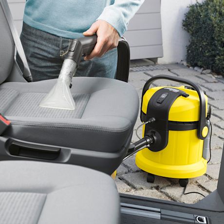 Henkilö puhdistaa auton harmaan istuimen keltaisella märkäkuivaimurilla