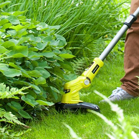 Limenvihreä ruohotrimmeri leikkaa nurmen reunaa tiheän kasvuston vieressä.
