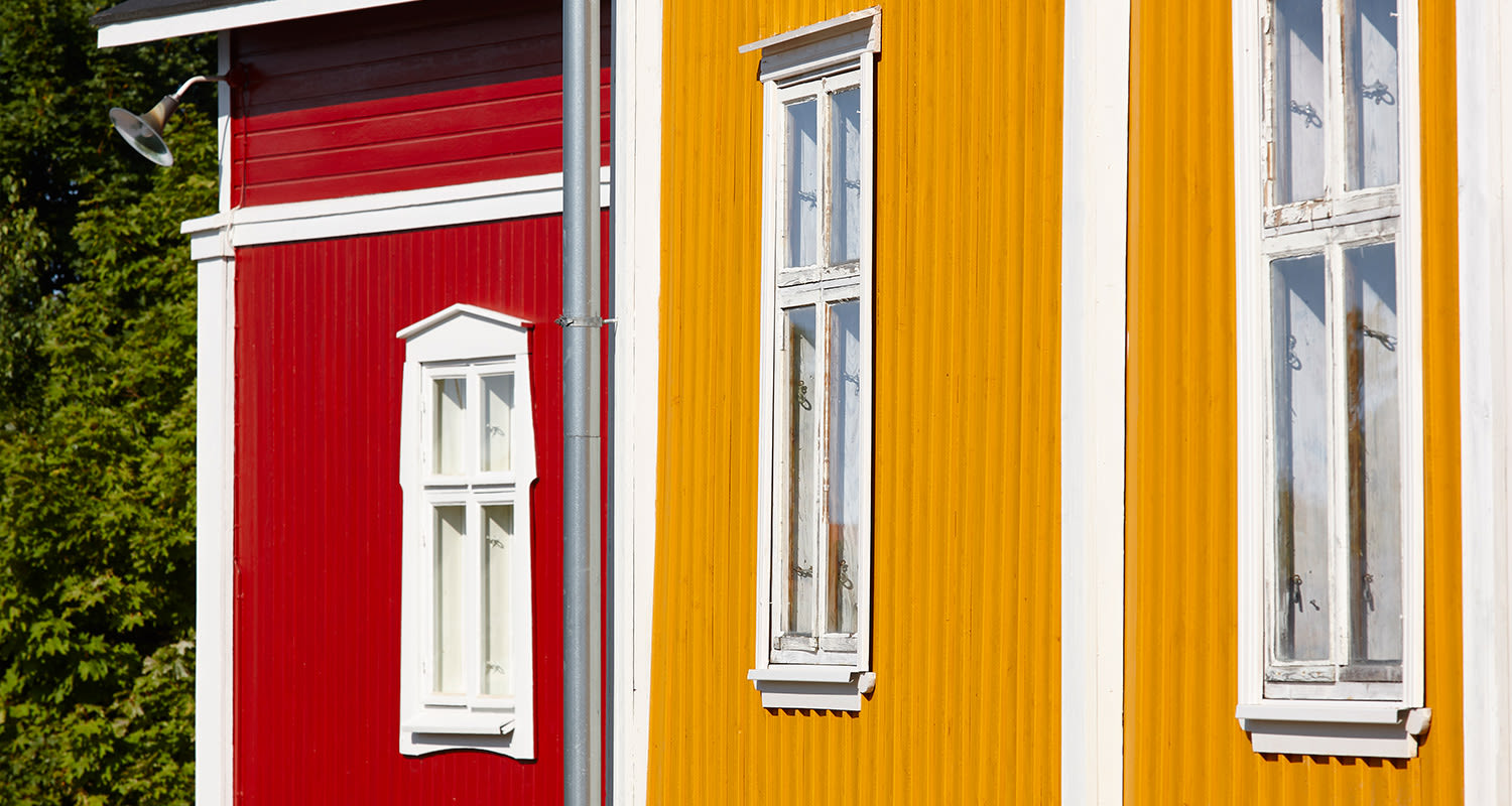 Punaisen ja keltaisen puutalon seinät, valkoiset ikkunat ja niiden välissä harmaa putki