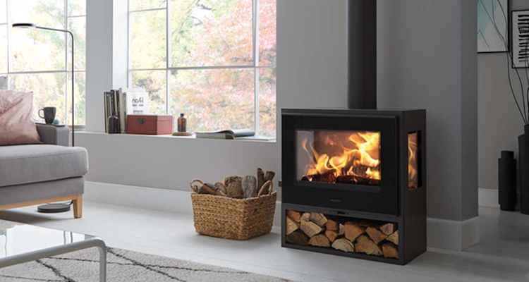 Harmaa olohuone, musta takka liekkeineen, korillinen halkoja ja syysvärinen ikkunanäkymä