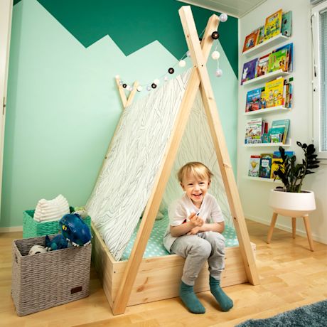 Lapsi puisessa teltanmuotoisessa vuoteessa mintunvihreässä lastenhuoneessa, lelukori ja kirjahylly.