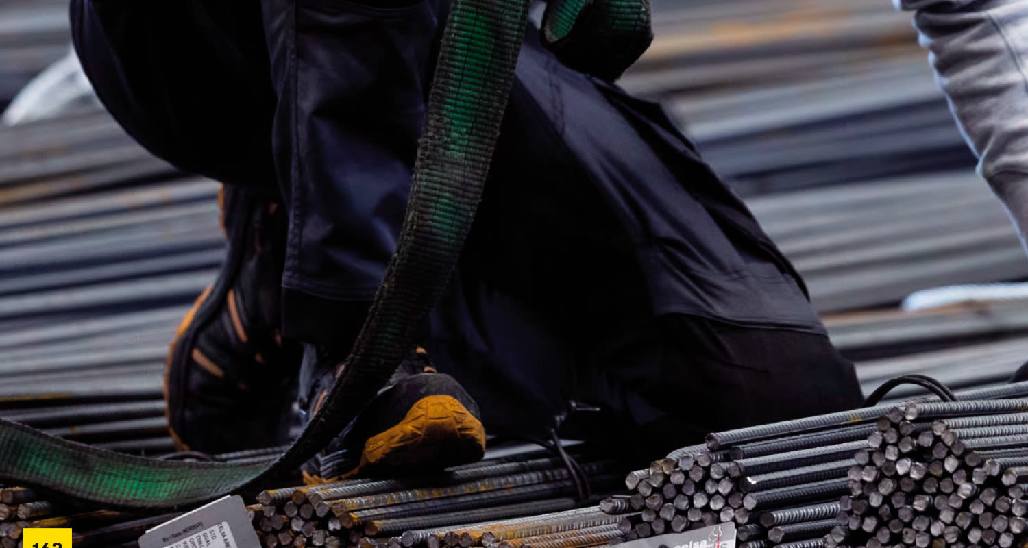 Työmies mustissa housuissa polvillaan kiinnittää vihreän nostovyön harmaisiin teräsnippuihin.