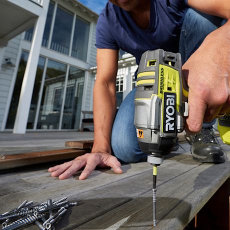 Mies ruuvaa puulautaa ulkoterassilla kelta-vihreällä Ryobi-porakoneella.
