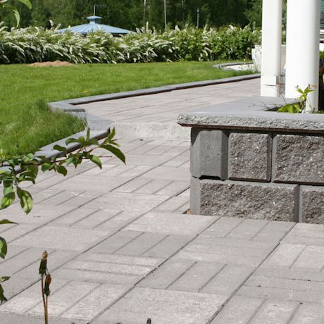 Harmaa betoniterassi tummanharmaalla reunakivellä, taustalla nurmikko ja valkoiset kukkapuskat