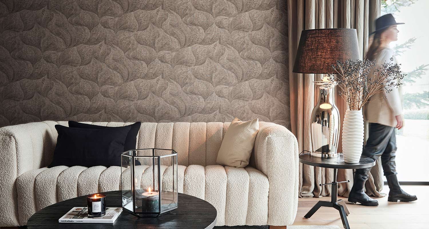 Kuvan olohuoneessa sohvan takana näyttävä ruskeasävyinen tapetti BN Riviera Maison 3 221143. Tuotetta myy K-Rauta