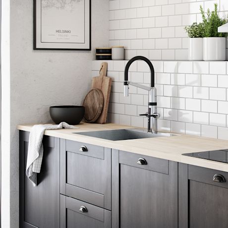 Moderni keittiö, vaalea puutaso, harmaat kaapit, teräsallas, valkoinen laattaseinä, leikkuulaudat, yrtit.