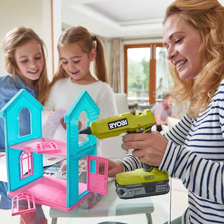 Nainen ruuvaa turkoosin-pinkkiä nukketaloa vihreällä akkuporakoneella olohuoneessa.