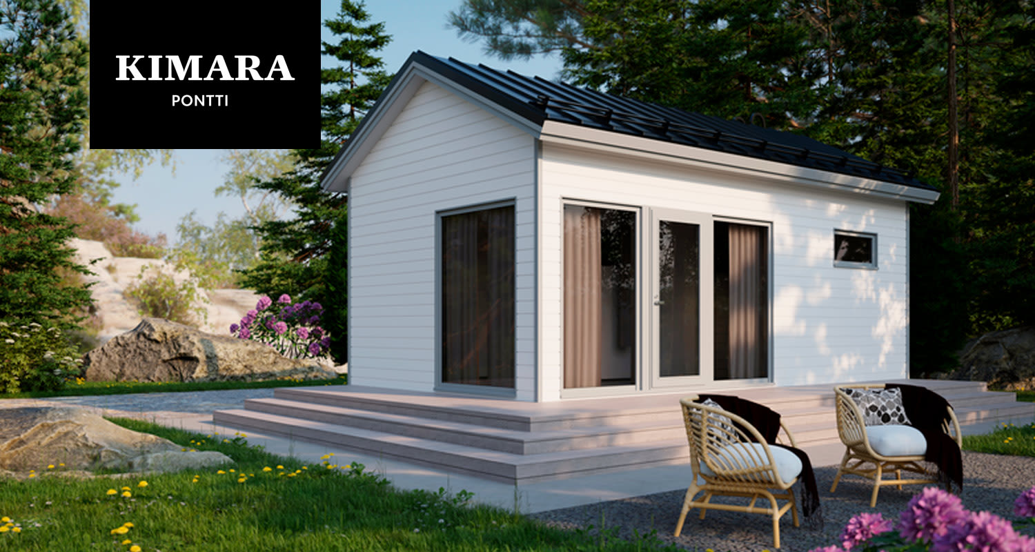 Valkoinen pikkumökki mustalla katolla metsän reunassa, terassilla rottinkituolit ja lilat kukat.