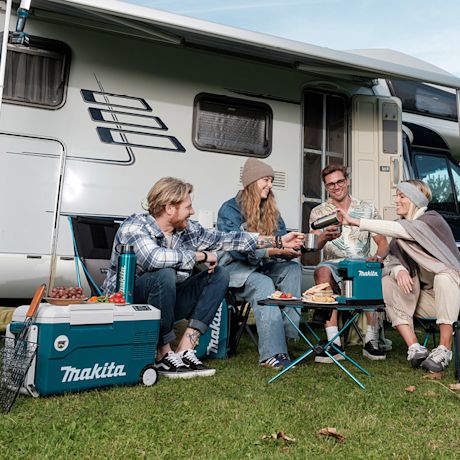Ihmiset istuvat ruohikolla valkoisen matkailuauton edessä ja maistelevat kahvia Makita-välineillä.