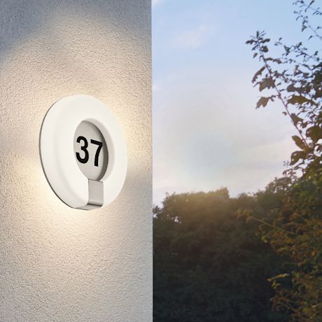 Valkoinen pyöreä seinävalaisin mustalla numerolla 37, himmeä valo ja taustalla puiden siluetit