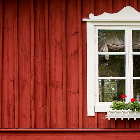 Punaisen puuverhouksen keskellä valkoinen ikkuna, pelargonit ikkunalaudalla