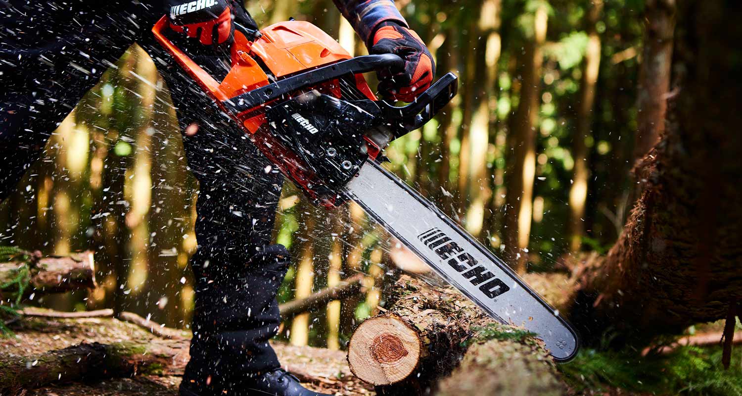 Oranssi ECHO-moottorisaha sahaamassa puunrunkopalaa metsässä, puunsirut lentävät