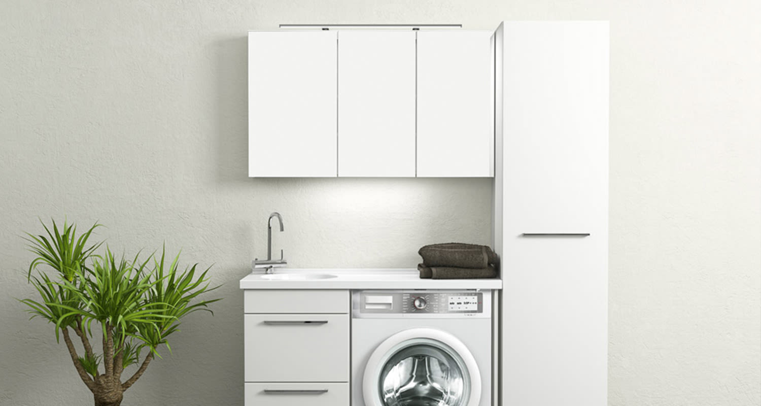 Valkoiset kaapit, pesukone, allas ja kromihana, tummat pyyhkeet ja viherkasvi.