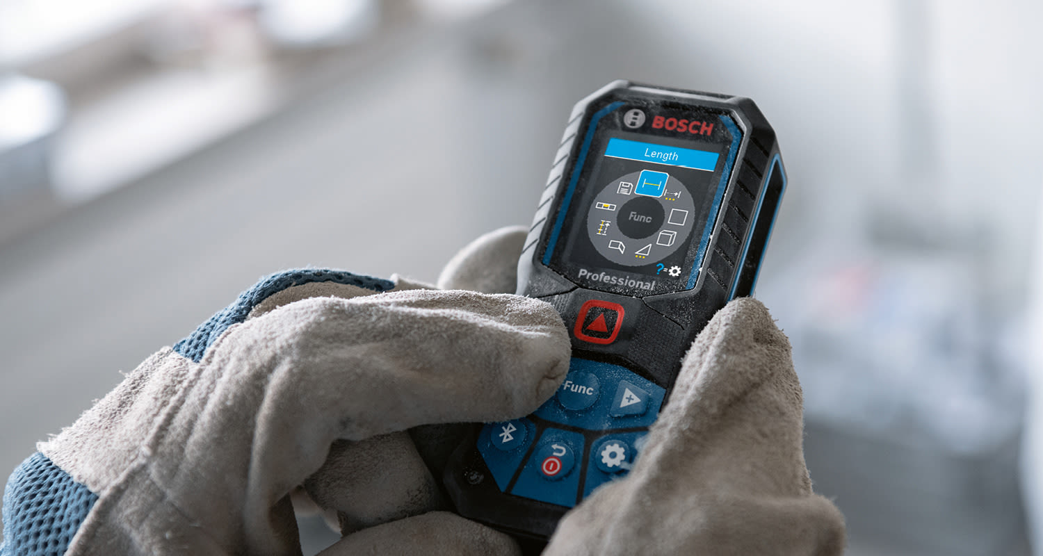 Harmaat-siniset työhanskat pitelevät Bosch Professional -lasermittaria kirkkaalla mittausnäytöllä