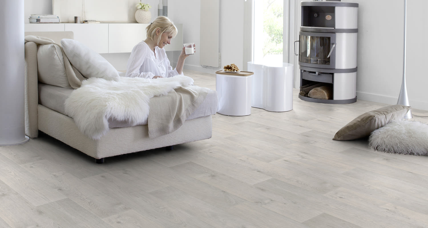 Vaalea muovimatto vaaleassa modernissa olohuoneessa, jossa nainen juo maitoa isolla sohvalla