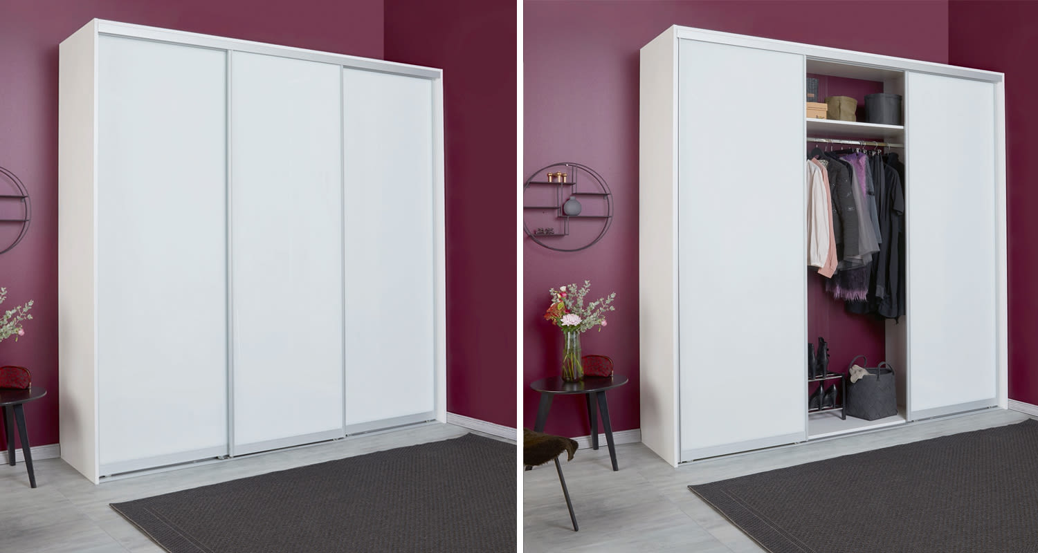 Valkoinen liukuovikaappi violetin seinän edessä avattuna vaatteille, vieressä musta kukkapöytä.