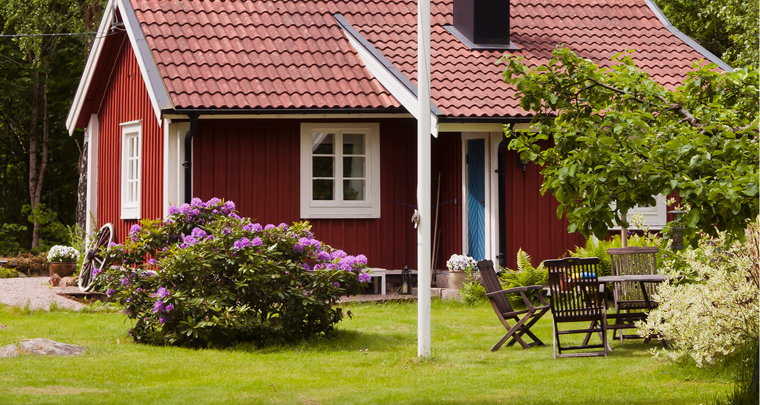 Kaunis punainen mökki ja hoidettu nurmikko.