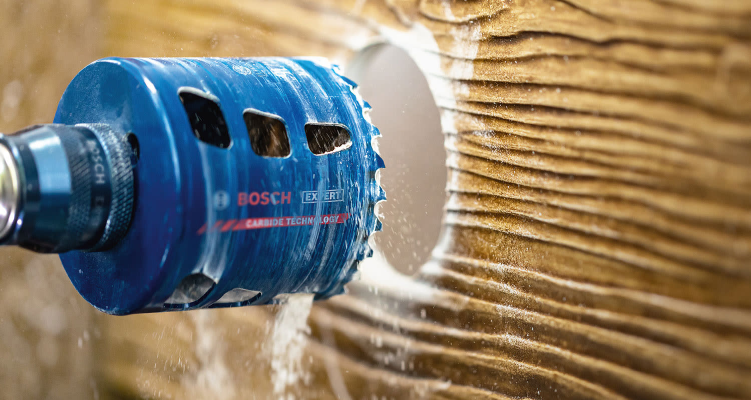 Sininen Bosch Expert -rei’itysterä poraa pyöreää reikää ruskeaan syykuvioiseen puuhun, purua leviää